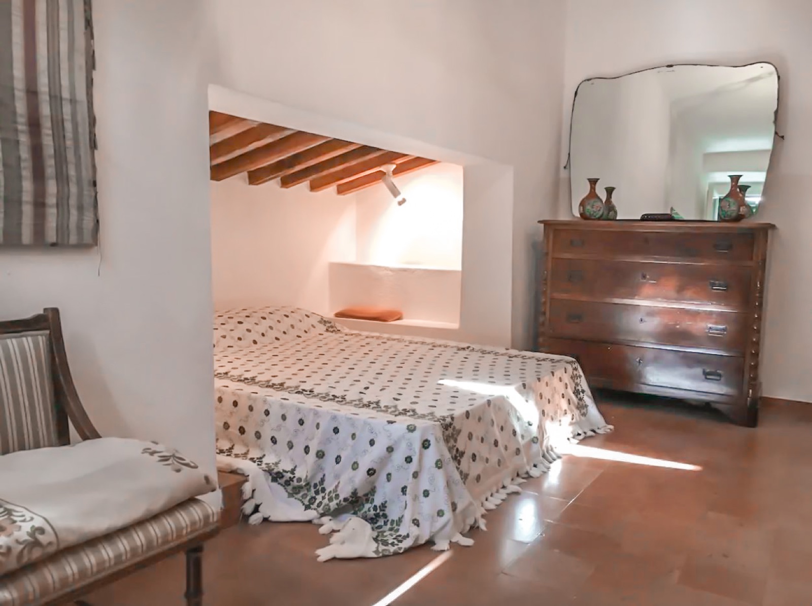 A bedroom with an antique chest of drawers and a mirror